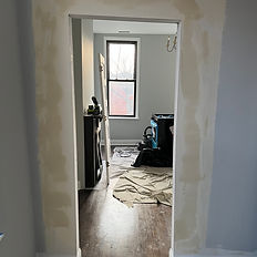 Interior drywall patching in progress with plastic floor protection and tools visible — Rock Bottom Restoration pre-paint prep work.