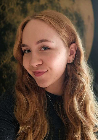 A young woman with her head tilted to the left, smiling at the camera. She has blonde, wavy hair and a black shirt.