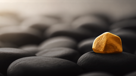 One warm-gold stone rests in sharp focus among softly blurred charcoal stones, representing the choice to direct our attention toward what is true and life-giving.