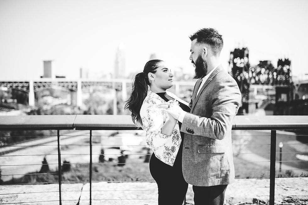 Man and woman stand with their hands held with Cleveland bridges in the background