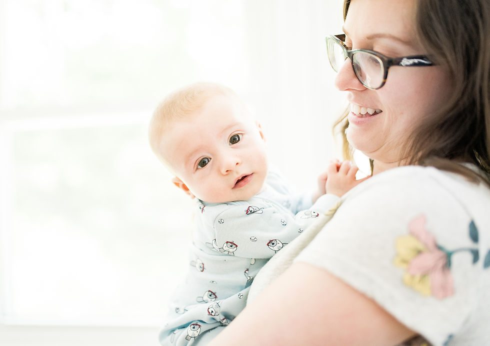 Mom smiles and holds baby near a light filled window
