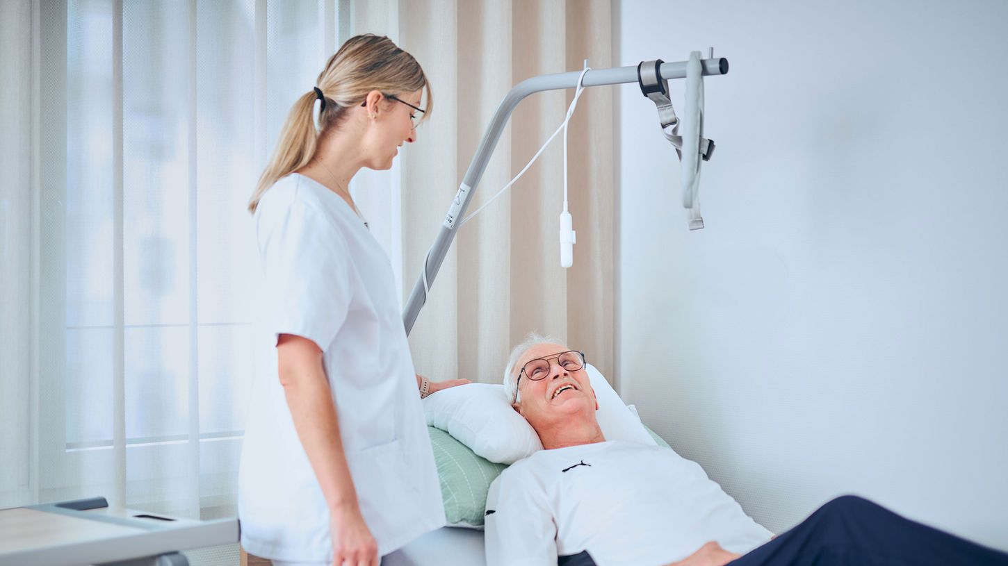 Patient nutzt Bettgalgen zur Mobilisation, begleitet von Pflegekraft am Krankenbett