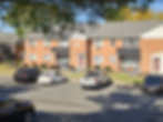 Exterior photography of a brick apartment building. Cars are parked in the lot under a clear sky, depicting a residential scene.
