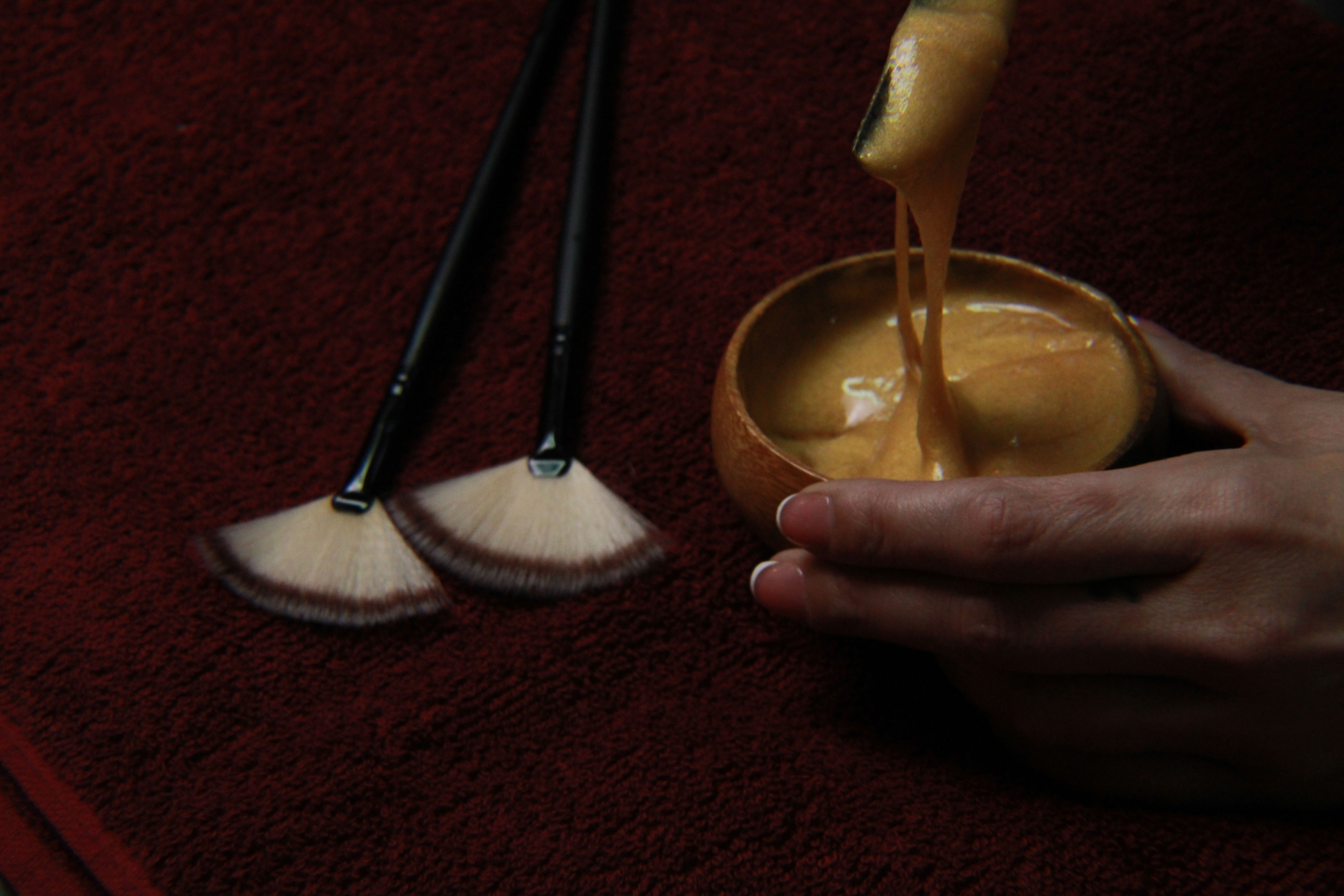 Hand mixing golden substance in bowl, fan brushes.
