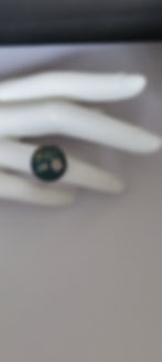 Bague avec fleurs blanches sur fond vert, portée sur une main blanche.