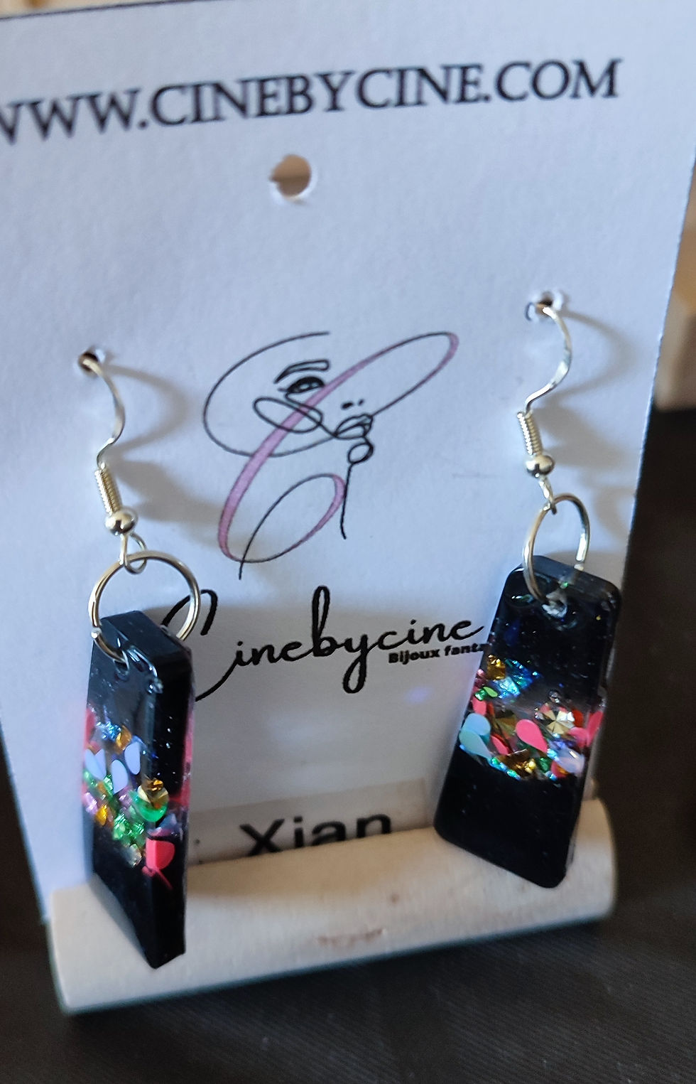 Boucles d'oreilles noires, texte 'cinebycine' et 'Xian', détails colorés, bijoux faits main.