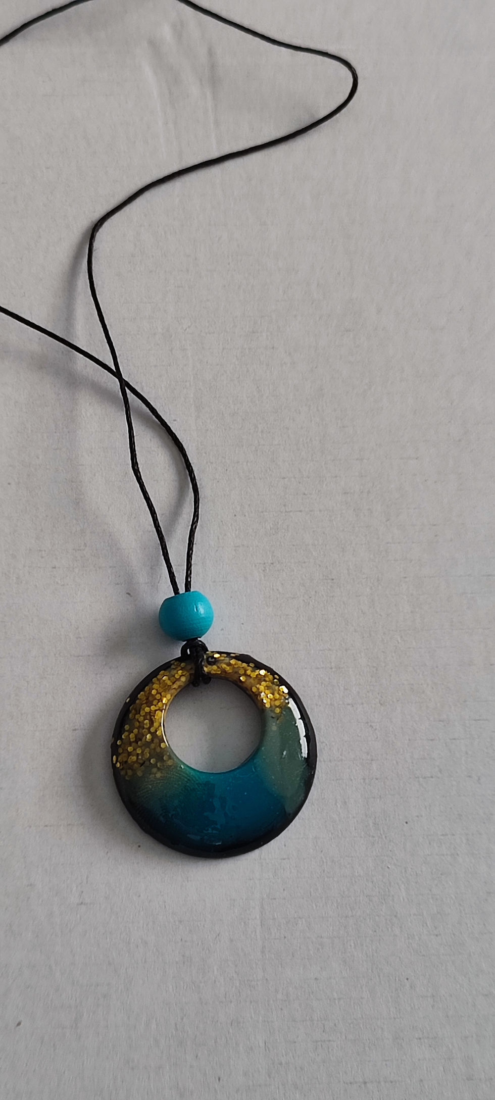 Pendentif rond bleu et or, avec cordon noir et perle turquoise. Détail d'un bijou.