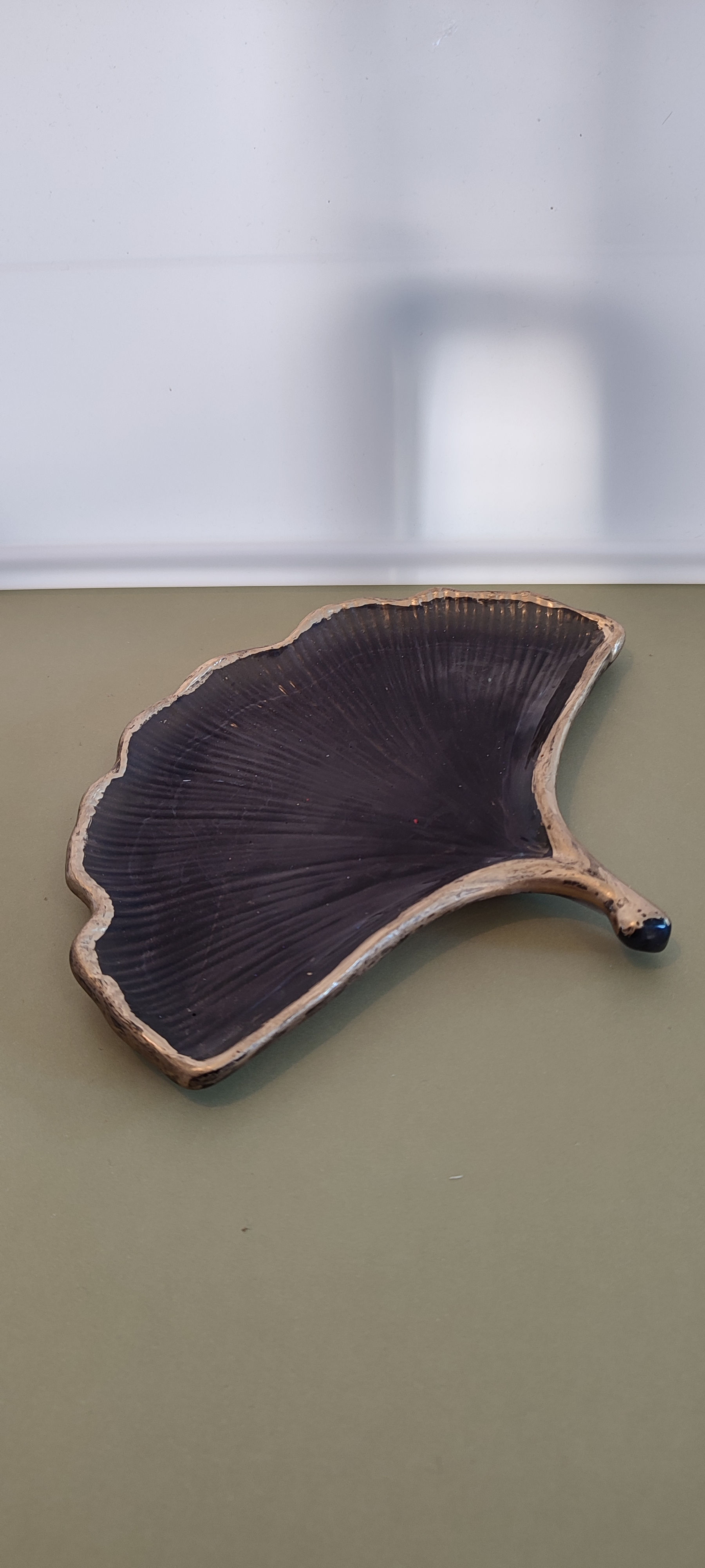 Une sculpture en forme de feuille de ginkgo brun, sur un mur vert clair.
