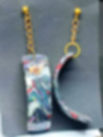 Boucles d'oreilles pendantes avec des motifs colorés et des chaînes dorées sur fond noir.