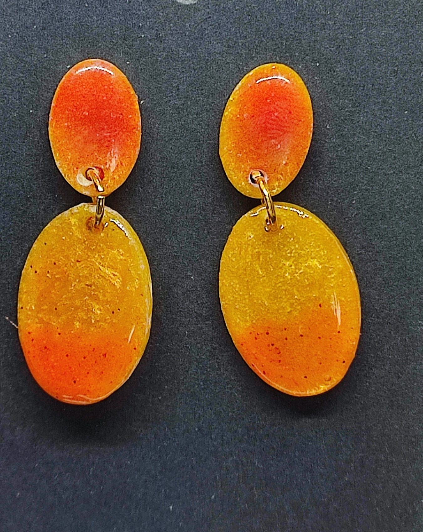Boucles d'oreilles pendantes ovales, orange et jaune, sur fond sombre. cinebycine