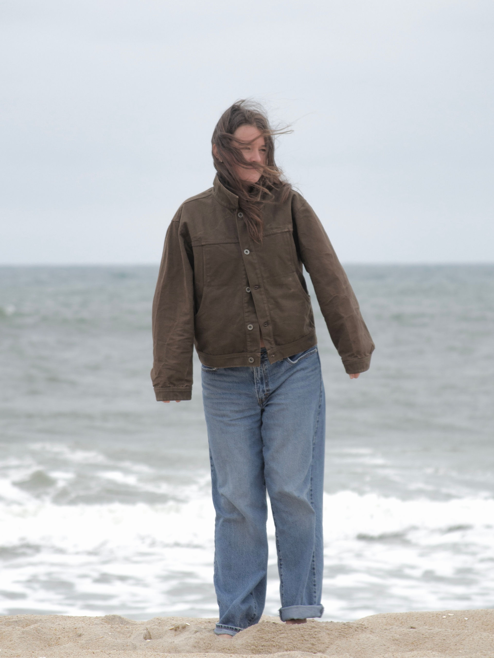 woman wearing a brown jacket on the beach by the ocean