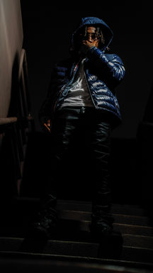 Person in dark hooded puffer jacket standing dramatically in darkness.