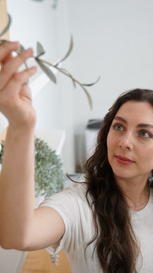 Woman gently touches delicate plant leaves in a bright room.