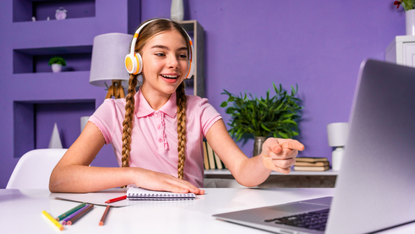 Young girl with headphones smiling and pointing at a laptop during an online class.