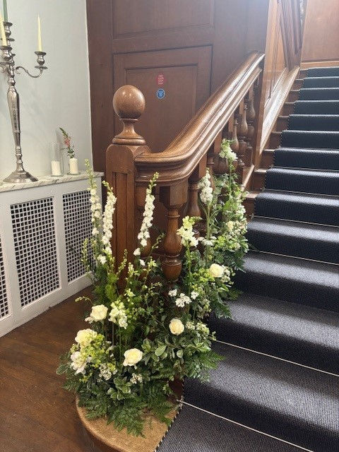 Floral arrangement of greenery and tall white flowers weaving up the stairs.