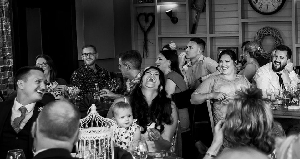 Candid black and white shot of bride and guests smiling during speeches, captured in a Hertfordshire wedding