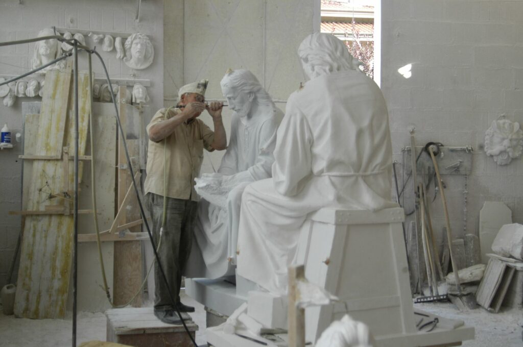 The image shows a master carver from Pietrasanta with both the plaster carver's model as well as the in process marble sculpture. Notice how St. Joseph's hands are still surrounded in stone.