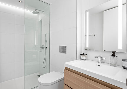 Modern bathroom in a modular home with glass shower, floating vanity, and illuminated mirror.