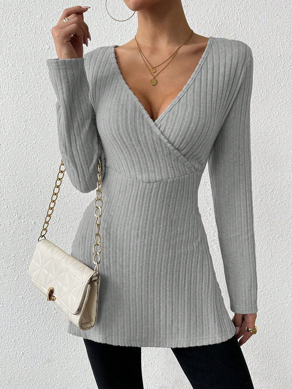 A woman taking a selfie, wearing a beige long-sleeve sweater with a crossover neckline and side slit, paired with black pants