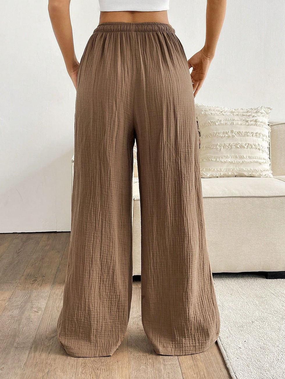 White wide-leg pants made of textured fabric with a drawstring waist, worn by a woman standing against a white wall, paired with a cropped top and black sandals