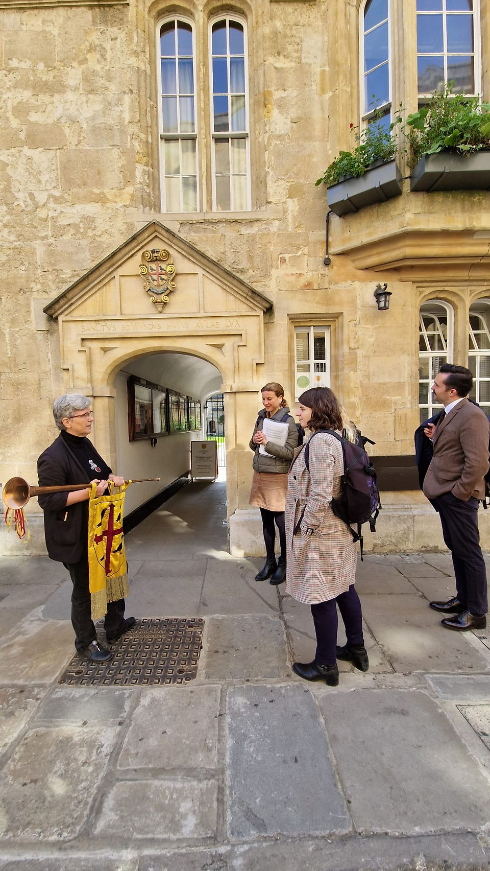 Mehrere Personen vor dem Eingang von St Edmund Hall, eine Person hält eine Trompete mit Banner in der Hand
