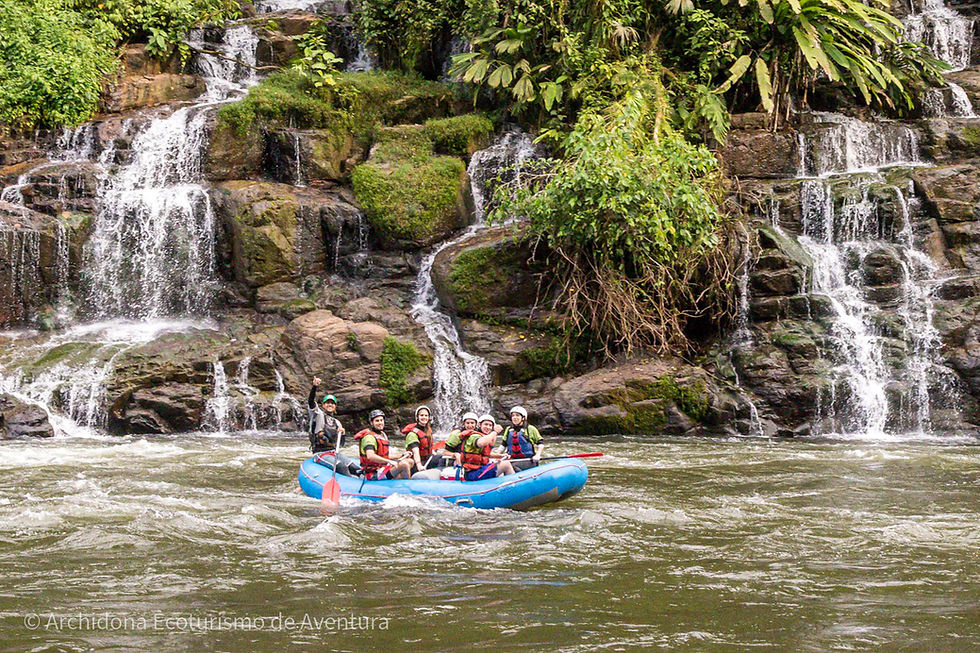 Un grupo de turistas emocionados haciendo rafting por el río Hollín, saludando con alegría frente a una hermosa cascada, disfrutando de la adrenalina y la belleza natural en armonía.