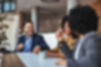 Three professionals smiling and having a friendly discussion at a modern office table.