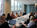 A group of professional women engaged in discussion around a conference table in a modern, well-lit meeting room with city views.