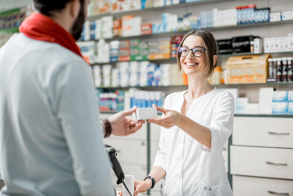 Smiling pharmacist in a white coat handing medication to a customer at a pharmacy counter, with shelves of medical products i