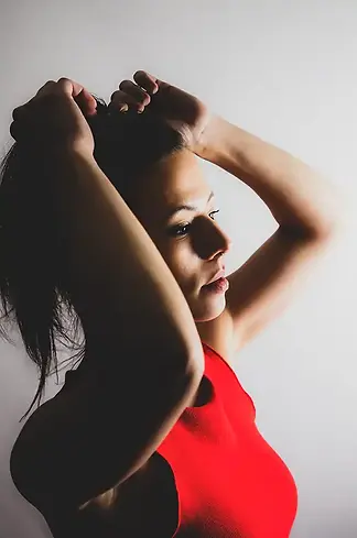 Un portrait d'une femme sur fond blanc ayant ses mains dans les cheveux. Elle porte un robe rouge