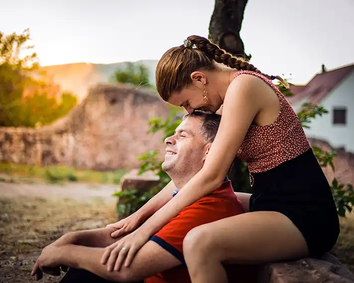 Portrait d'un couple assis l'un derrière l'autre. La femme fait un bisous sur la tête de l'homme