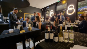soirée de degustation de vin dans un restaurant (Les Arcades) avec convives assis et debout ainsi que 5 bouteilles de vins rouges et blanc sur une table en premier plan