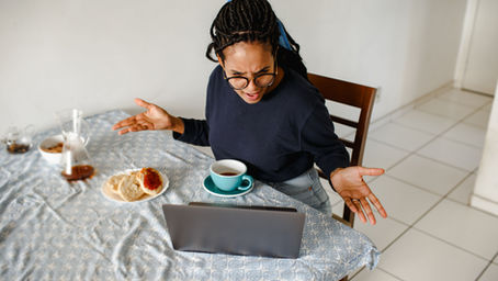 Woman having breakfast, looking angrily at open laptop