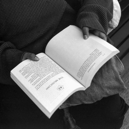 Black & white photo of a woman reading a book as she sits on a bench.