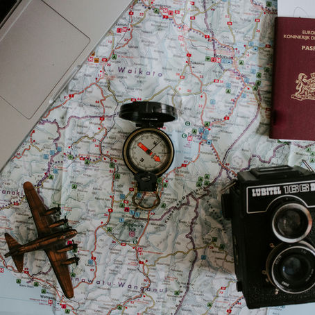A laptop, passport, camera and compass on top of a map of the world