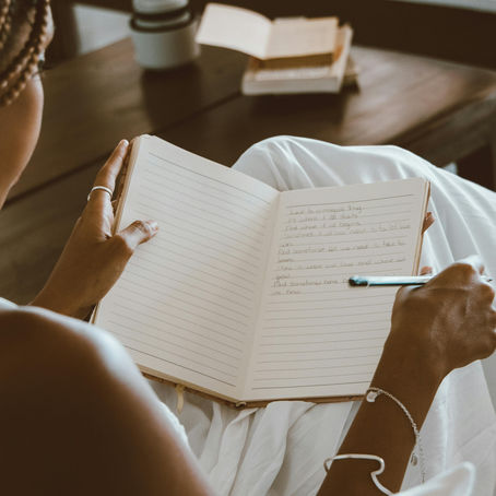 A woman sits on a sofa next to a coffee table and writes in her notebook