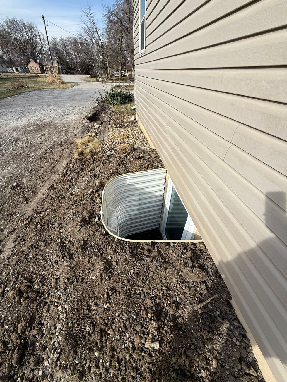 Angled exterior view of a newly installed basement egress window with enlarged window well and surrounding soil.