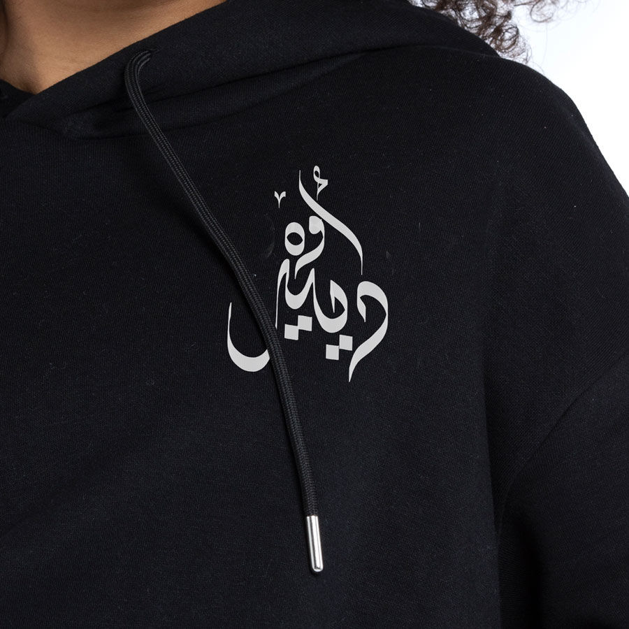 Thumbnail: Christmas White Deer Written In Arabic Calligraphy front view on a black hoodie close up