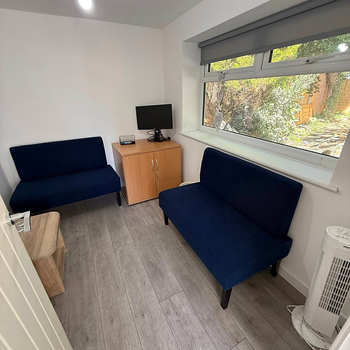 A small room featuring two blue couches facing a television on the wall