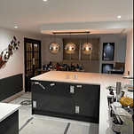 Modern kitchen under renovation, featuring a central island, pendant lights, and exposed cabinetry, cluttered with tools and materials.