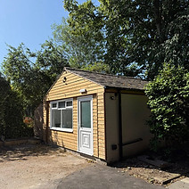 A small building with a car parked in front, showcasing a simple architectural design and a clear blue sky above