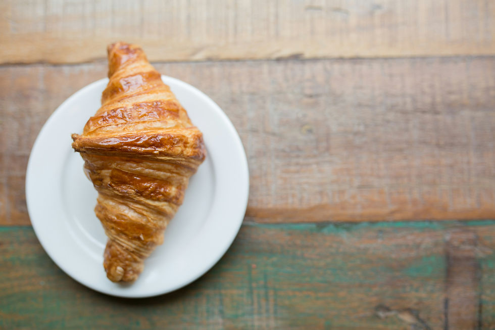 Ein Croissant auf einem weißen Teller, der auf einem Holztisch steht.