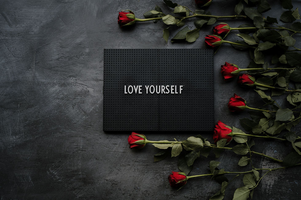 Eine Tafel auf dem Tisch auf der steht: Love yourself. Drumherum liegen rote Rosen