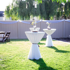 Two white cocktail tables on a green lawn, outdoor event ready.