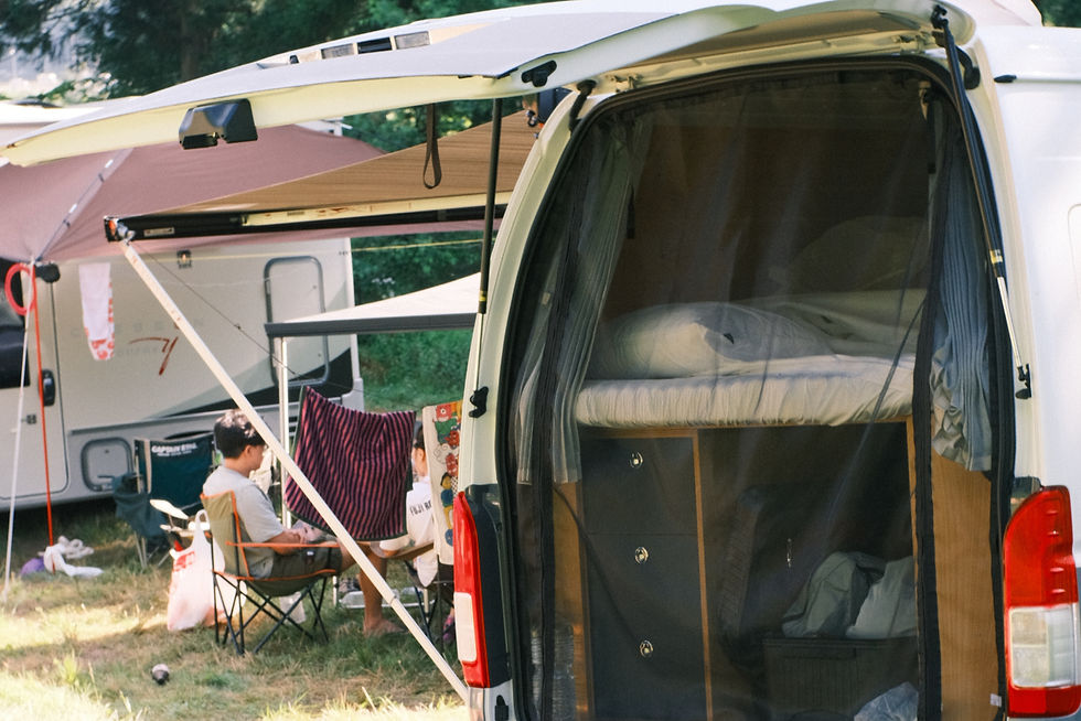 Open camper van with bed inside, people sitting outside under awning, towels hanging nearby. Sunny campsite with greenery in the background. Japan campervan, Tokyo campervan, Tokyo, vanlife, Japan road trip, camper van, fuji rock, japan summer