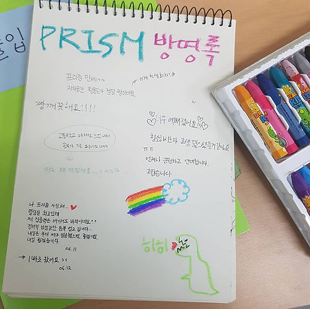 나무 책상 위에 크레파스와, PRISM 방명록이라고 크게 적힌 작은 스케치북이 있다. 그 아래 공룡 그림과 무지개 그림을 비롯한 다양한 글씨의 방명록이 적혀 있다. 내용은 다음과 같다. 프리즘 만세. 자치공간 활용도가 정말 짱이에요. 이게 학생회지. 짱 깨끗해요. 고등학교 야자실 느낌 나서 공부가 잘 되네요. 저는 왜 안 될까요? ㅋㅋㅋ 나 프리즘 사랑해. 하트. 열람실 최고인데 제 집중력은 여기서도 바닥이네요. 웃는 이모티콘. 정서적 안정감만 듬뿍 얻고 갑니다. 내일은 부디 제가 열공했으면 좋겠네요. 내일 뵙겠습니다. 6월 11일. 1빠로 왔어요. 6월 12일. 하트. 너무 예뻐졌어요. 하트. 청소하시느라 고생 많으셨을 것 같아요. 우는 이모티콘. 언제나 응원하고 연대합니다. 고맙습니다.
