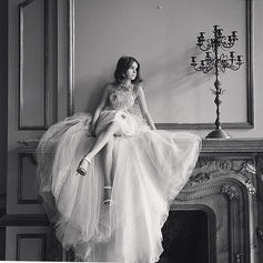 Elegant woman in flowing gown poses on an ornate fireplace.