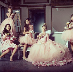 Five young girls in beautiful pink gowns posing elegantly in a grand room.