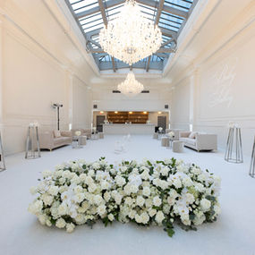 Grand white ballroom with floral centerpiece, chandeliers, and lounge seating.