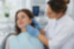 Dentiste en blouse blanche et gants bleus examinant l'articulation temporo-mandibulaire dâune patiente dans un cabinet dentaire lumineux.